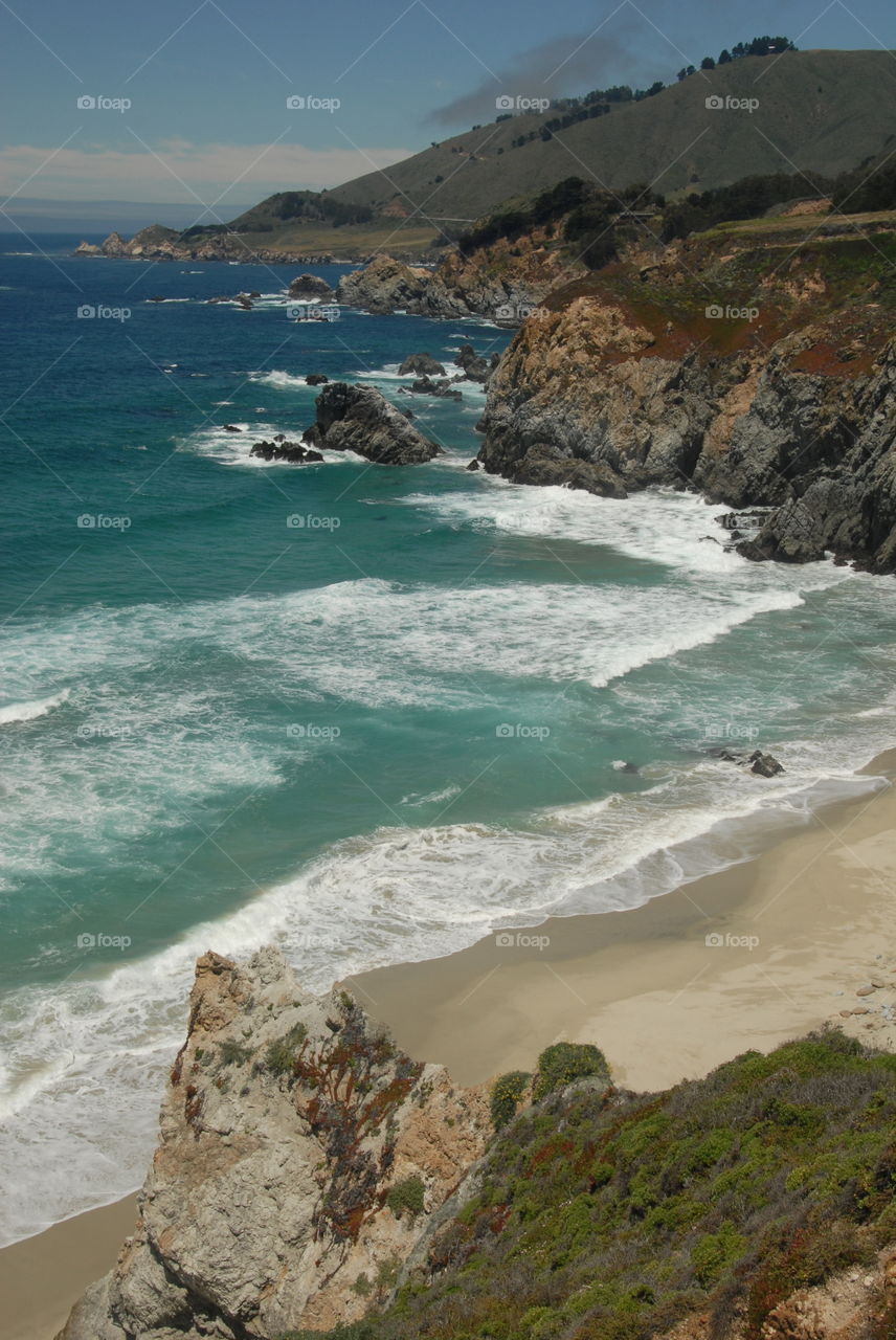 Looking down on a rugged beach with the white water of the waves crashing on the golden sand!