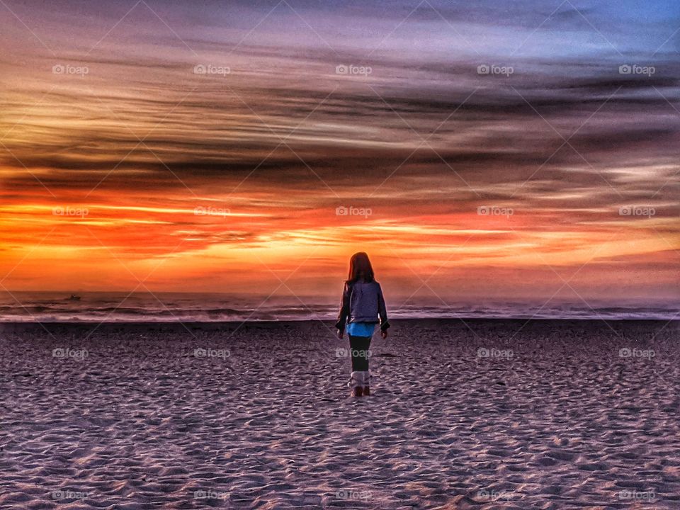 Capturing a young lady witnessing the amazing, bold and colorful sunset at the beach.