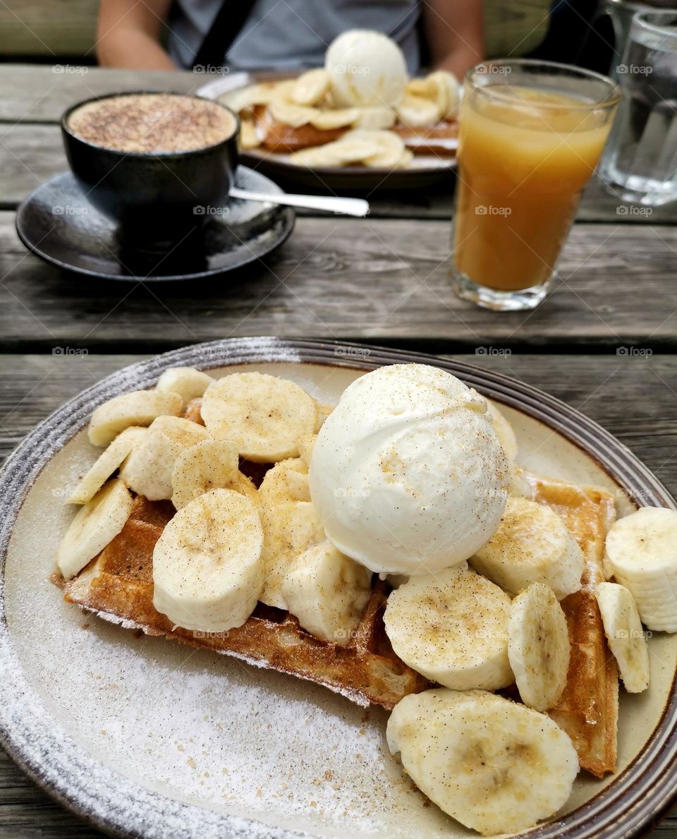 Delicious waffles with banana and ice cream. Cappuccino and orange juice. Tasty and yummy.