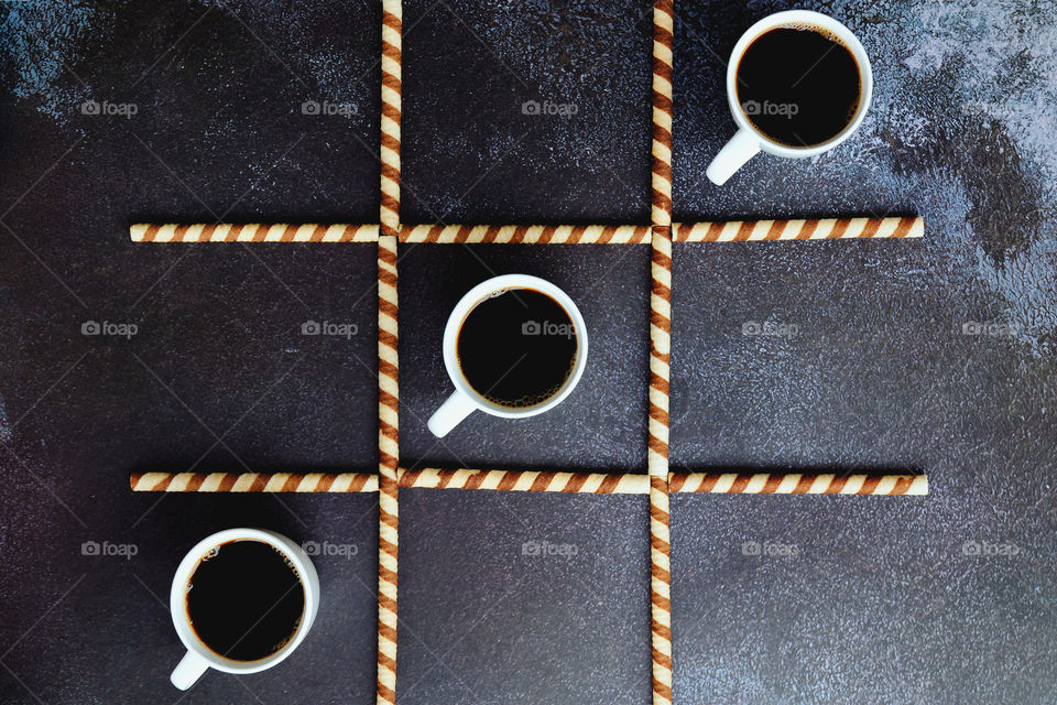 Business working morning with cup of hot coffee, sweet croissants on black background close up. Game of noughts and crosses. Top view, copy space, flat lay, mockup.