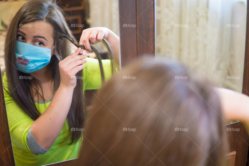 A young girl does makeup for a walk outside in a protective mask against the coronavirus pandemic, her lips are painted with red lipstick.
