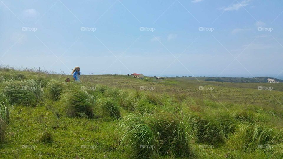Lone blonde biker girl explorating the  Transkei, walking in tall green grass. blowing in the wind
