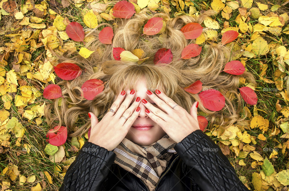 Elevated view of woman lying in autumn leaves covering face