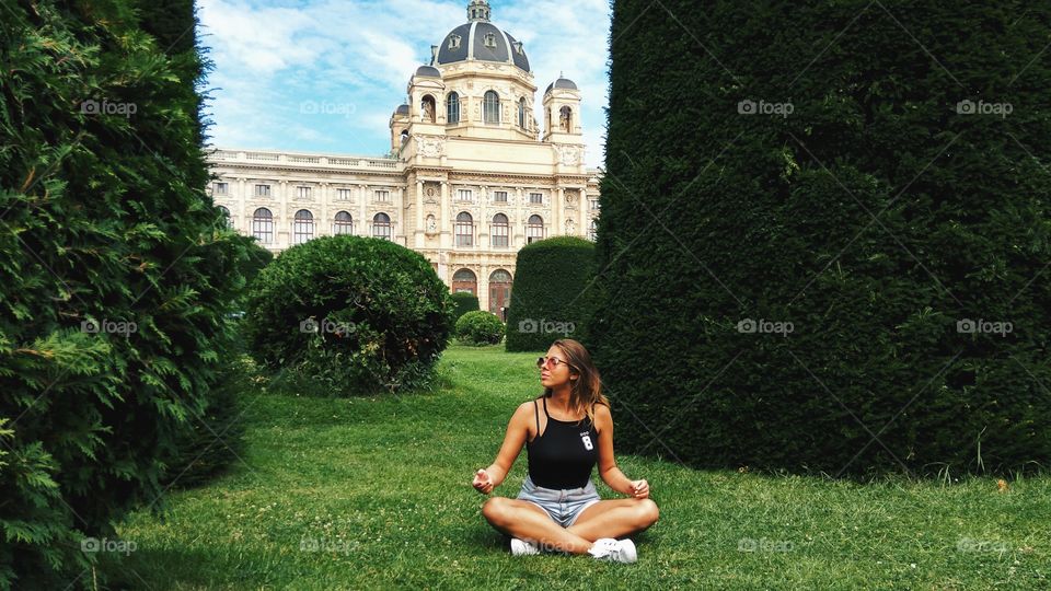 Woman meditating on grass in front of ancient building