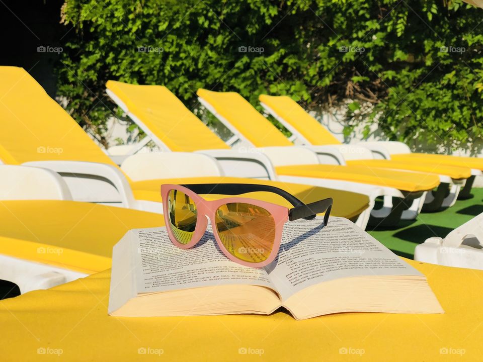 Pink sunglasses and a book placed on a yellow sunbed with many yellow sunbeds in the background