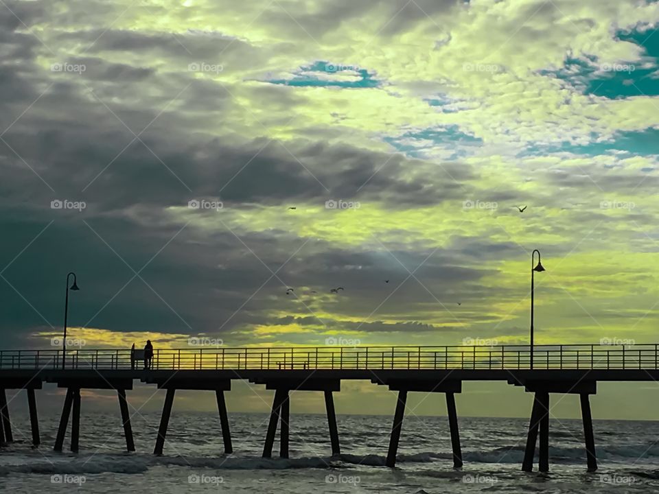 Jetty silhouette at sunset during storm golds and reds 