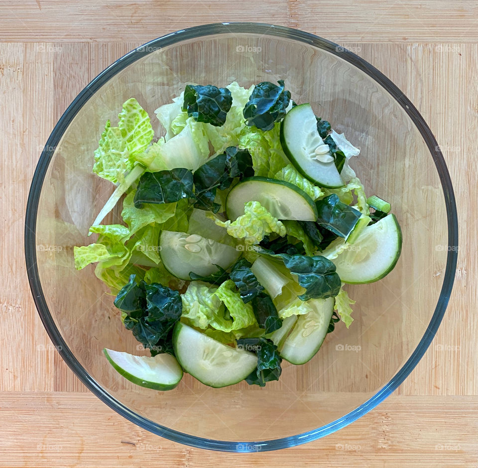 Green salad in a glass bowl on a wood cutting board