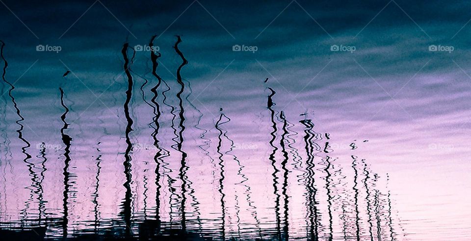 detail of boat masts reflection over sea at sunset