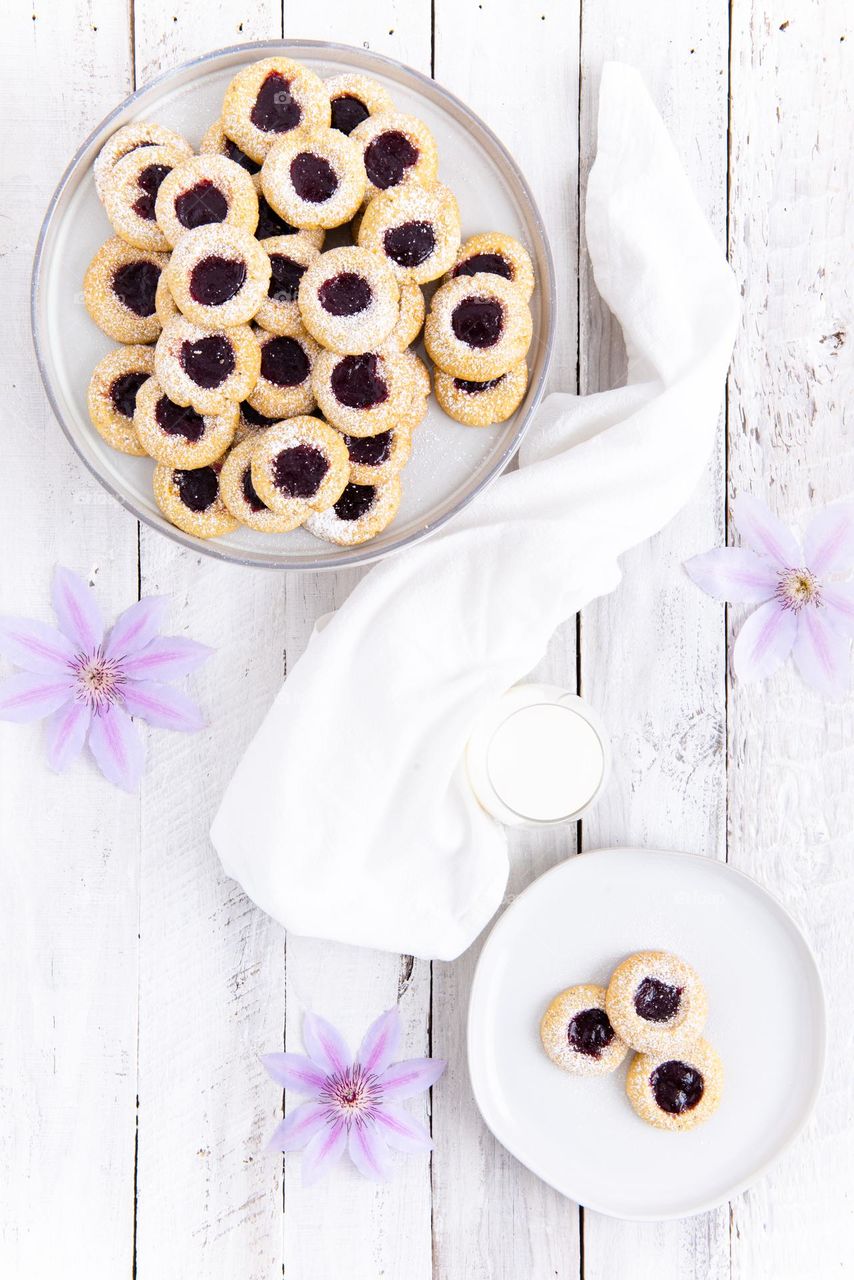 Bright flat lay of a plate of raspberry thumbprint cookies with a glass of milk 