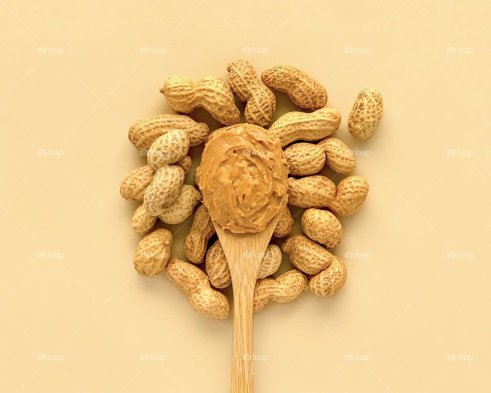 Peanut butter on wooden spoon, nuts on beige