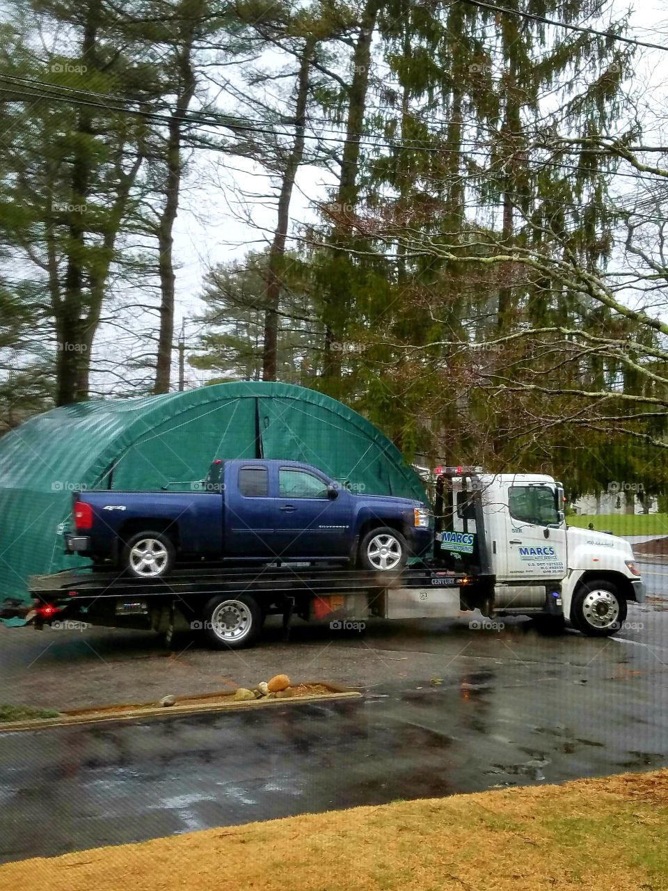 Pickup truck on flatbed tow truck leaving in rain to get repaired, vehicles are ready to go.