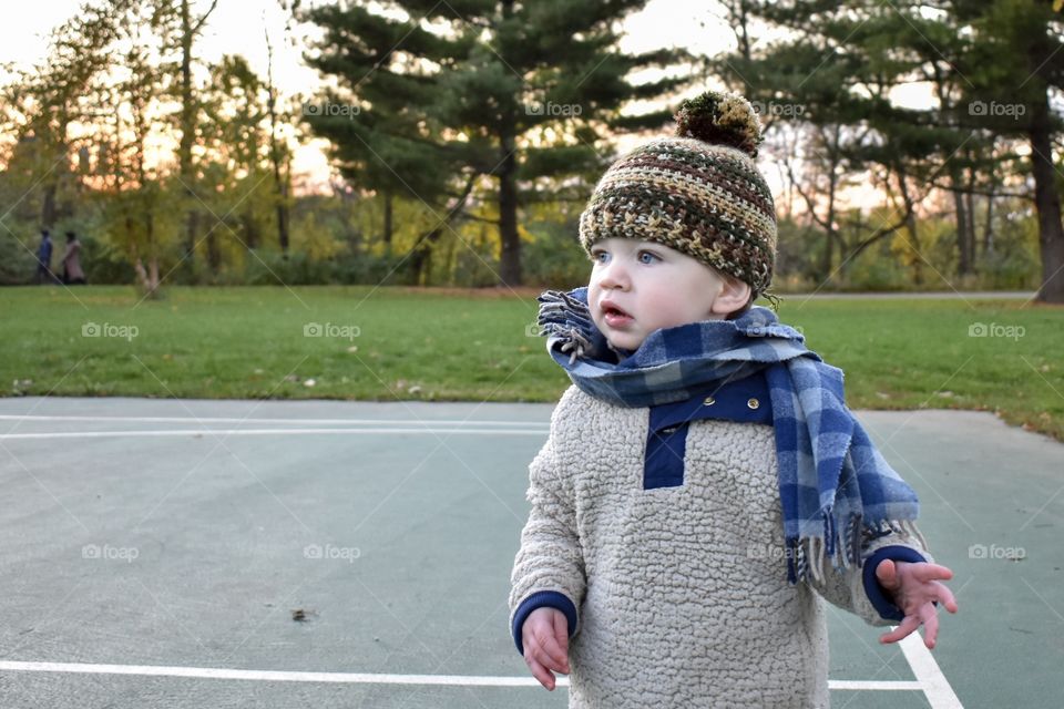 Cute toddler boy playing on basketball court during cold fall evening sunset 