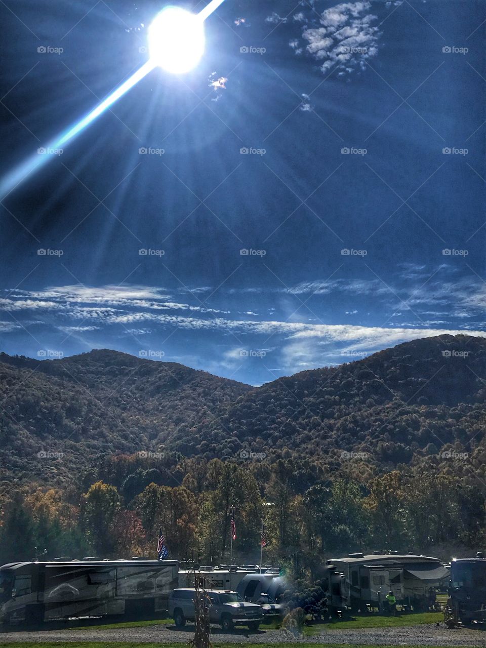 The suns rays and a few clouds over a mountain range with campground in foreground 