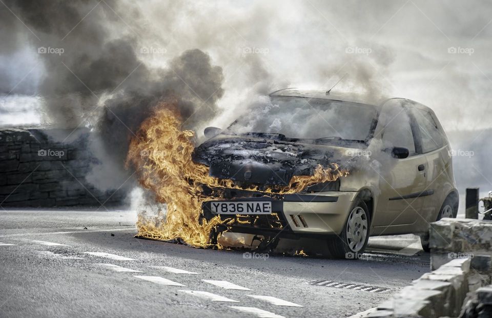 A car on fire in the road. 