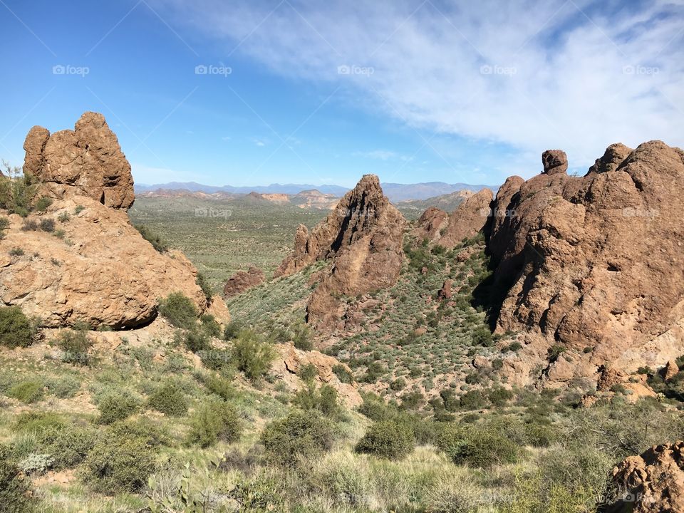 Desert mountain, looking down at the horizon; various green vegetation and blue skies with thin clouds