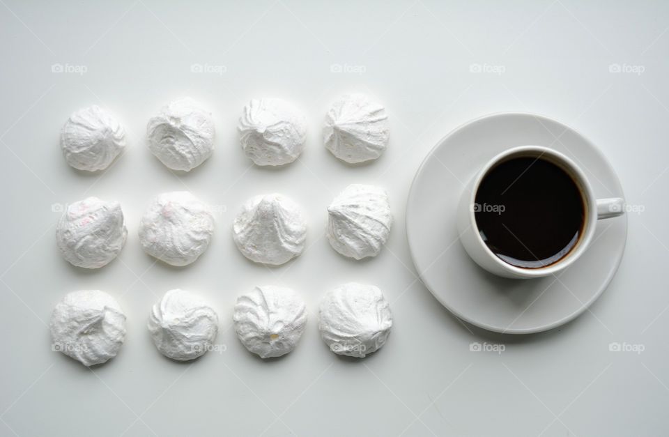 cup of coffee and sweet sugar meringues on a white background, beautiful texture top view