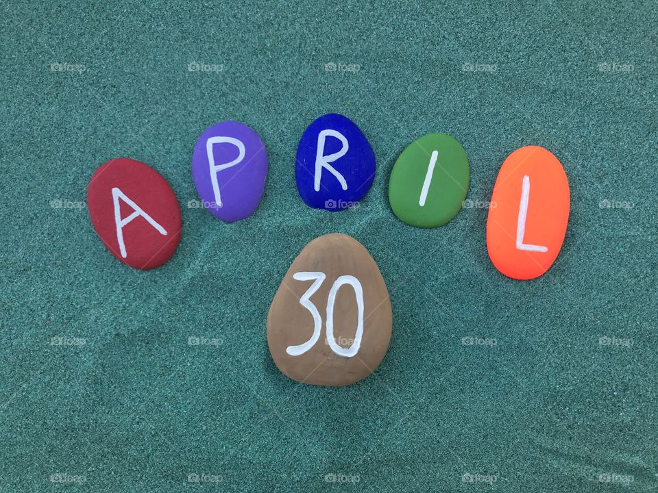 30 April, calendar date with colored stones over green sand 