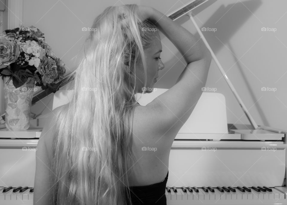 black and white image of a beautiful girl side profile face with long blonde hair wearing black sitting at a white piano running her fingers through her hair