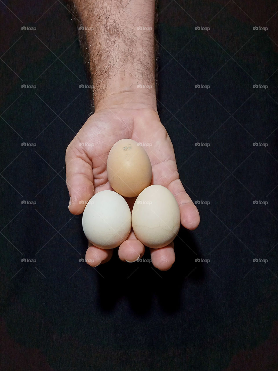 a human hand holding three eggs on a black background
