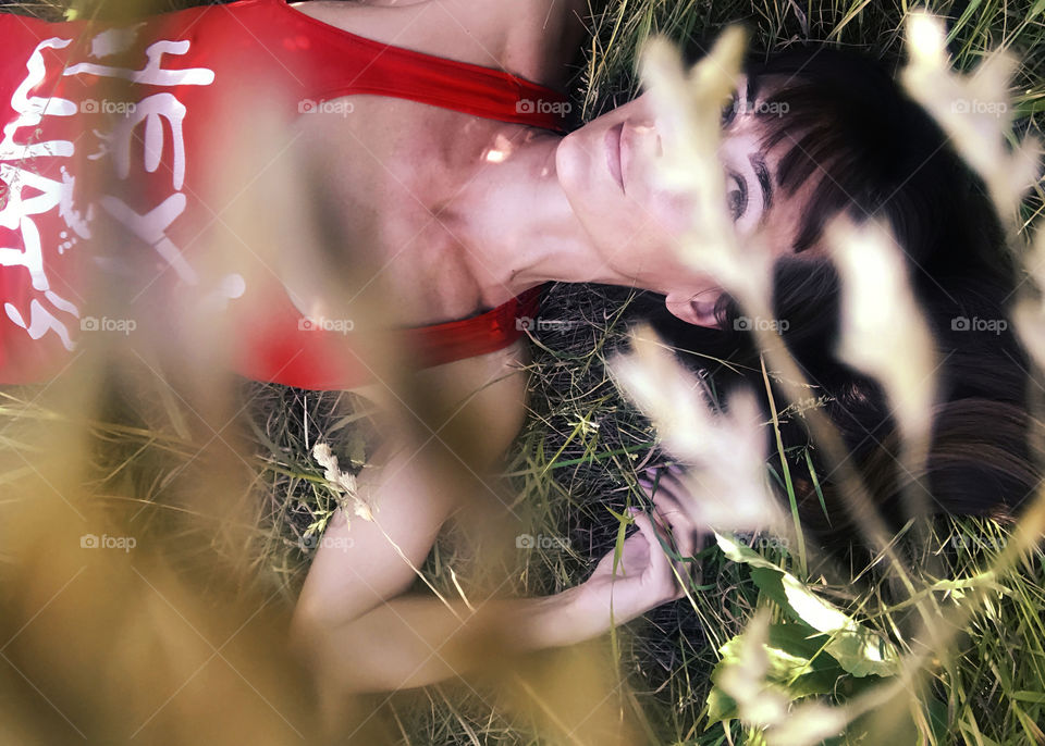 Young woman with long hair lounging on the grass in the summer field 