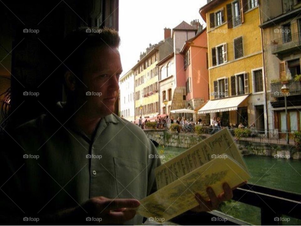 Man in restaurant in France with menu. Water. Canal. Buildings.