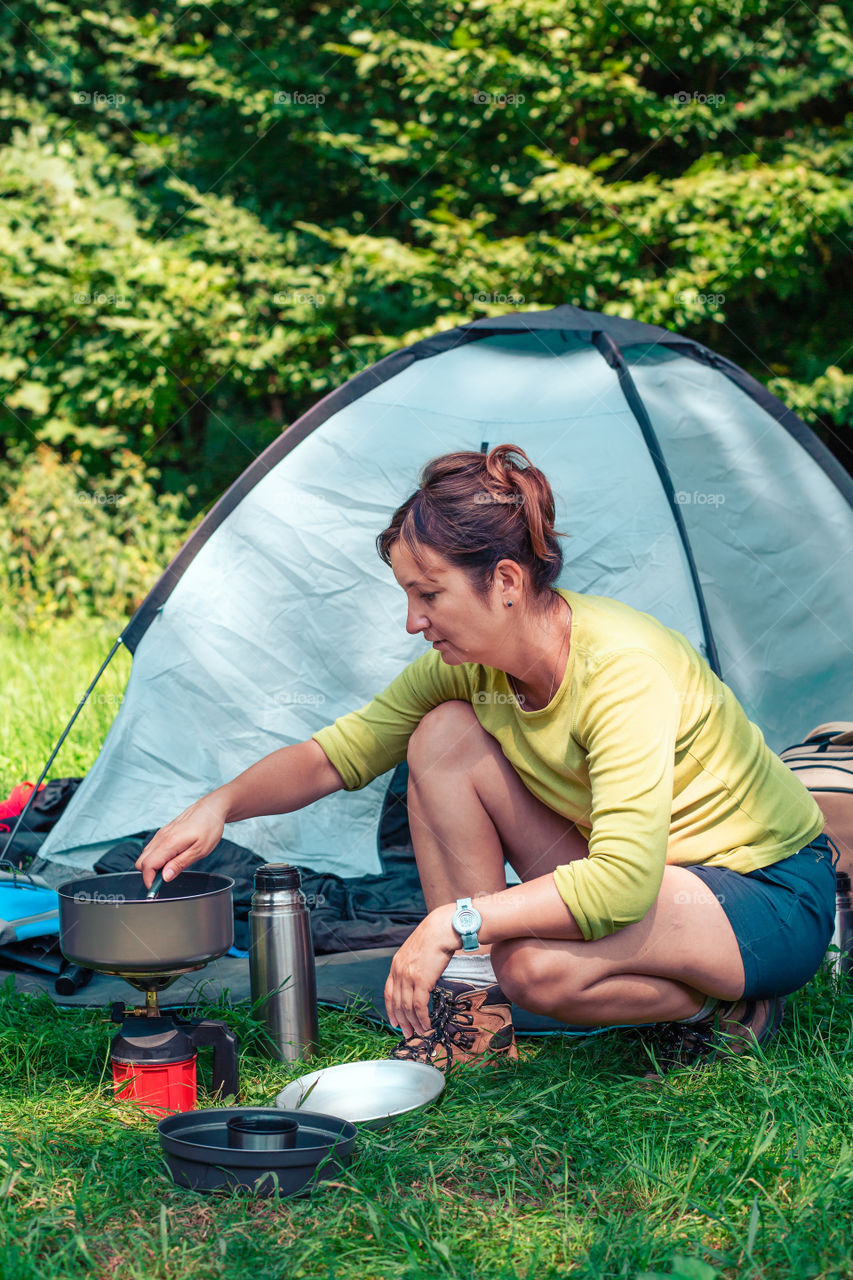 Spending a vacation on camping. Woman preparing a meal outdoor next to tent