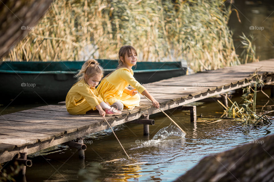 Little sisters playing near lake at autumn day 