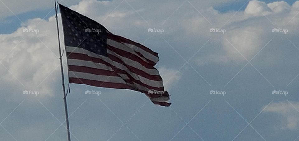 the clouds hide the blue sky & a large American Flag waves in wind symbolizing freedom & independence