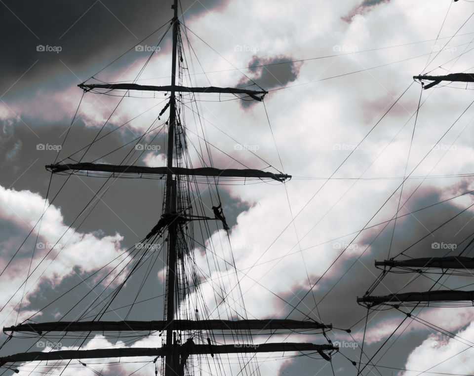 A black and white image of a mast of a ship, and a silhouetted worker 