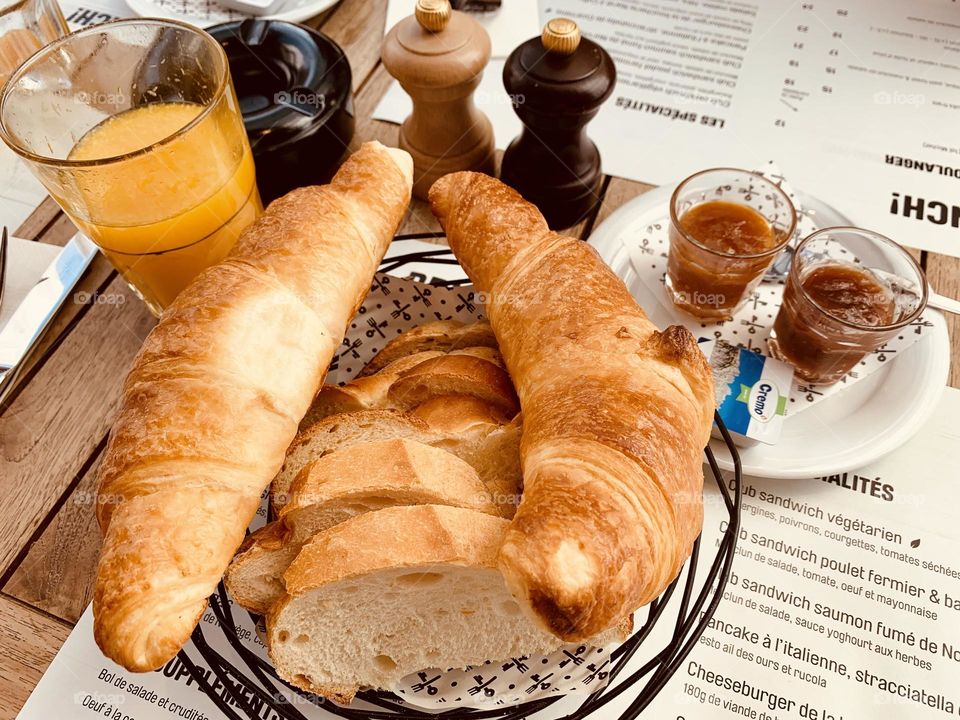 Basket containing freshly baked handmade croissant and slices of bread accompanied with orange juice and assorted jams 