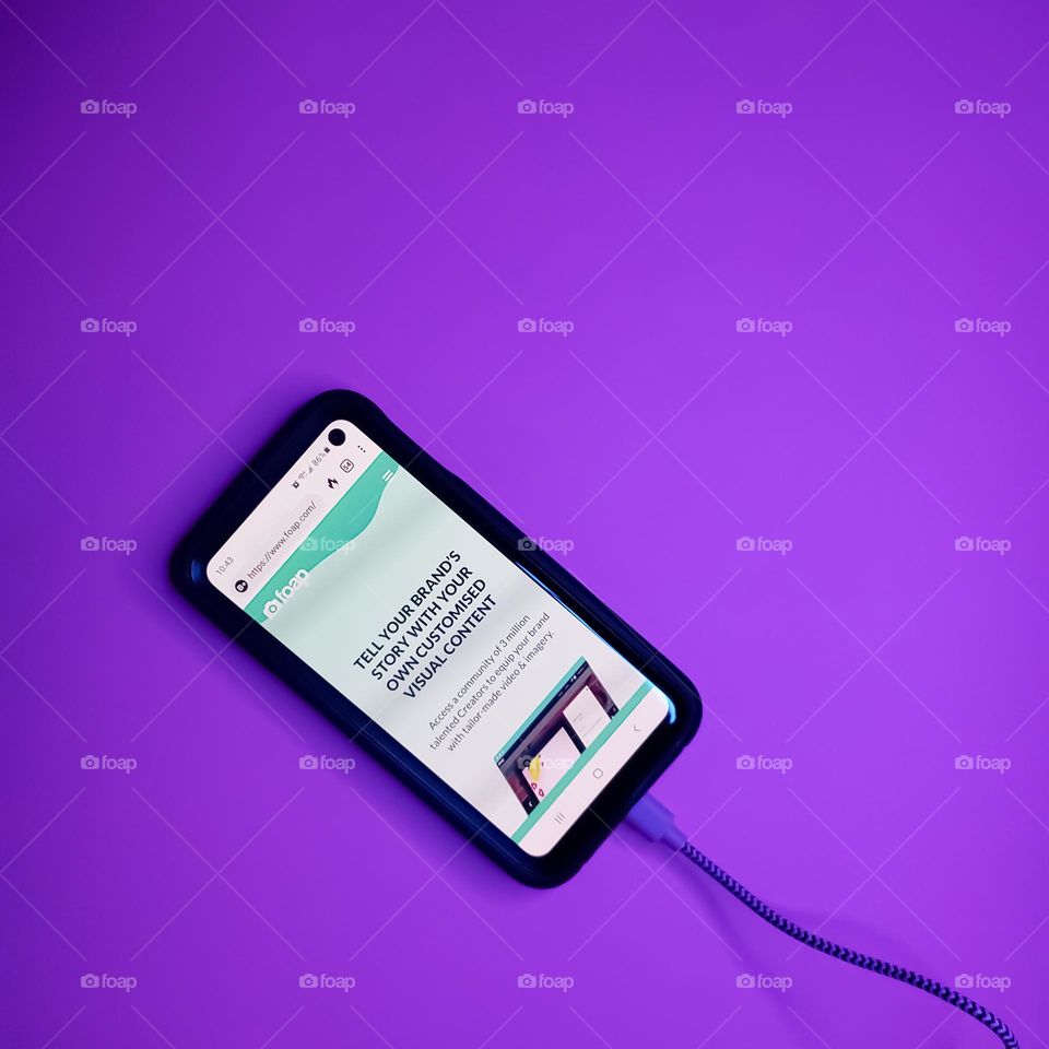 Mobile phone with FOAP website home page on a purple background connected to a purple USB charger.