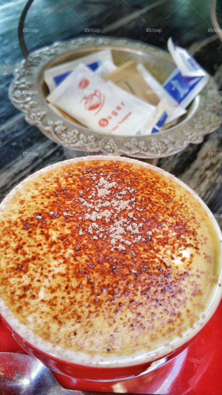 Cappuccino coffee with a selection of sugars in the background. Cappuccino is an Italian coffee beverage that is traditionally prepared with double espresso, and steamed milk foam.