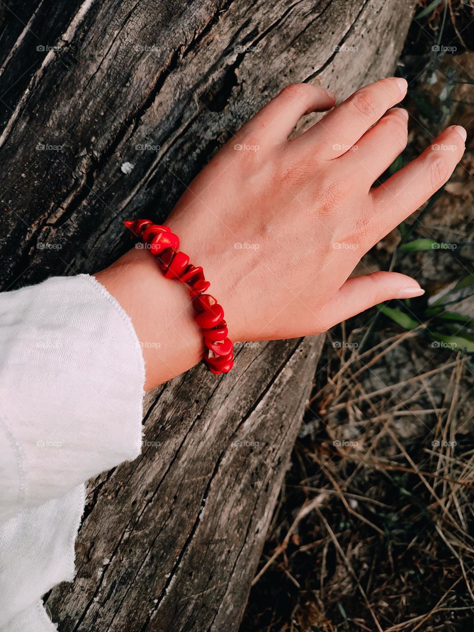 Woman hand in red stone bracelet on the wooden log