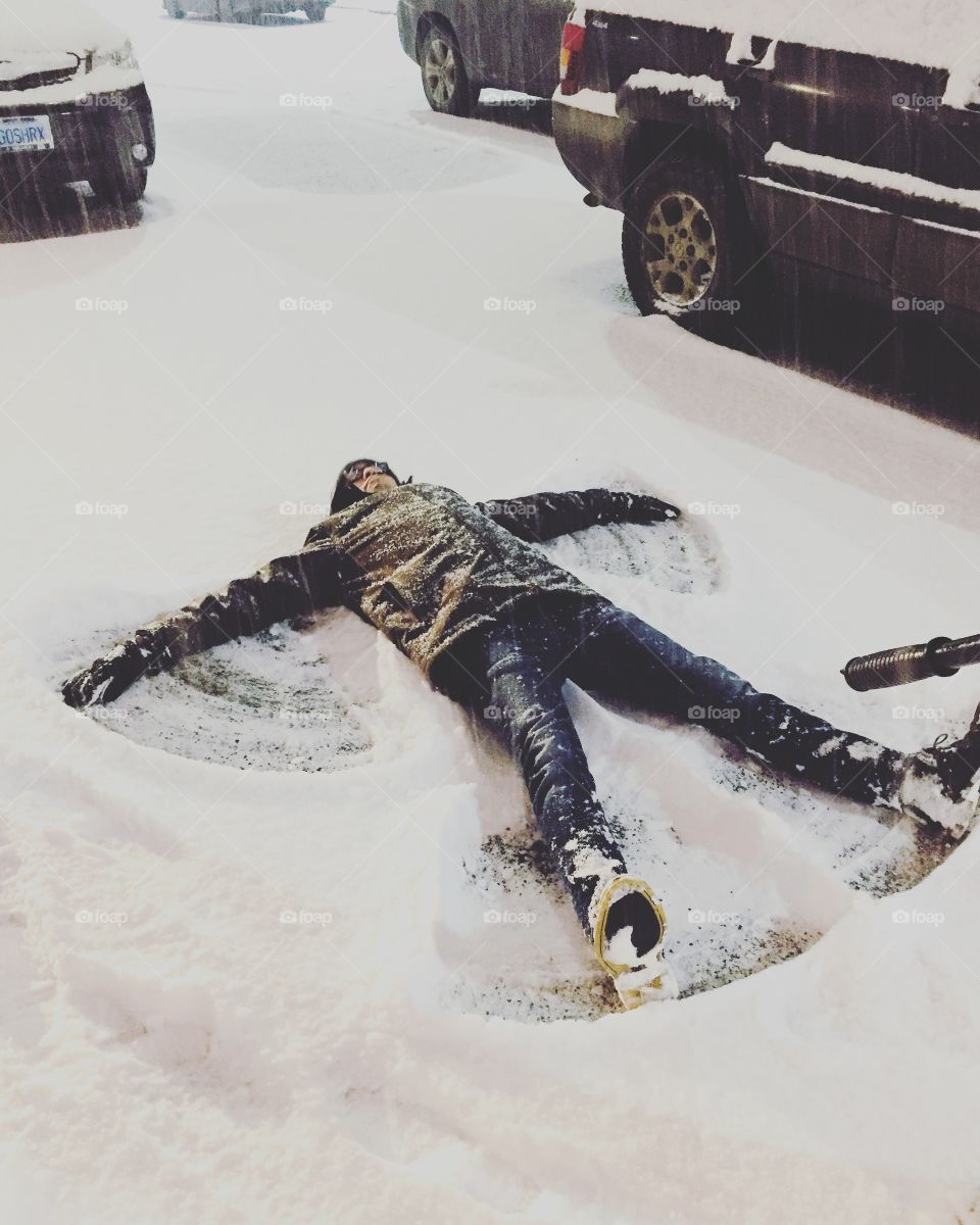 A young man making a snow angel for the first time after working in the middle of a parking lot.