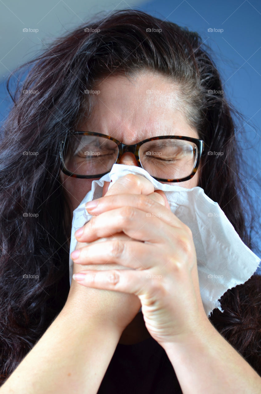Woman blowing her nose hard into a tissue at home