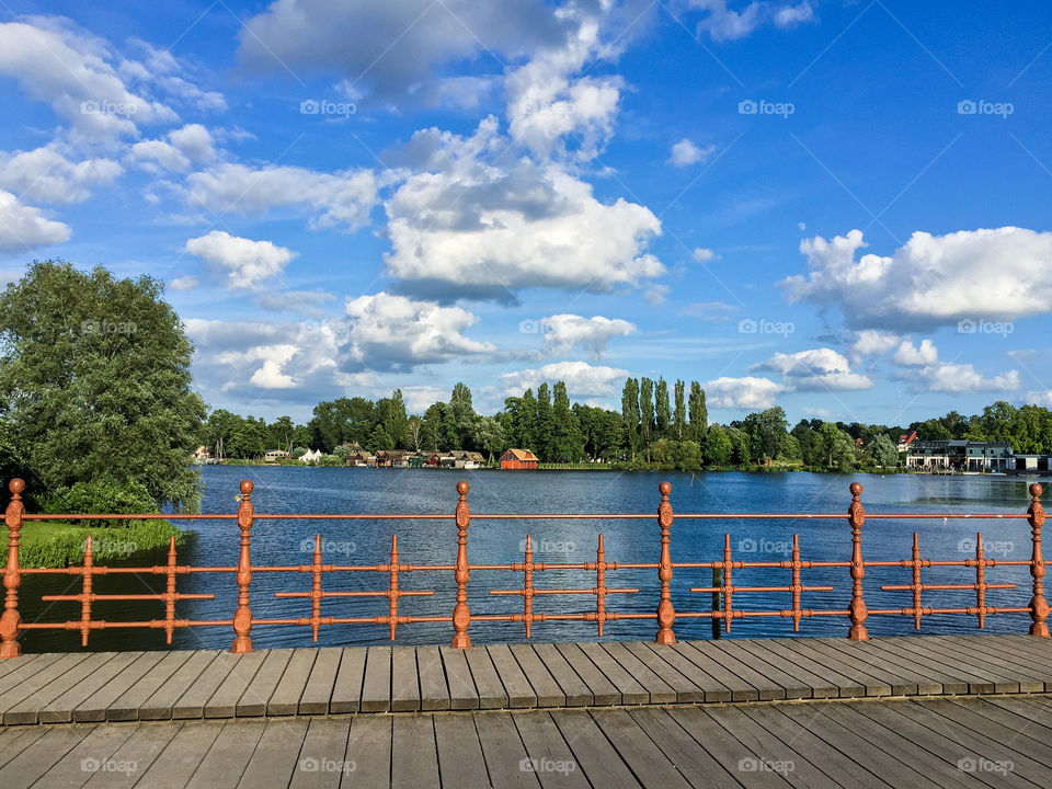 A wooden bridge with a brown iron fence in front of a lake in the Schwerin city in Germany in summer