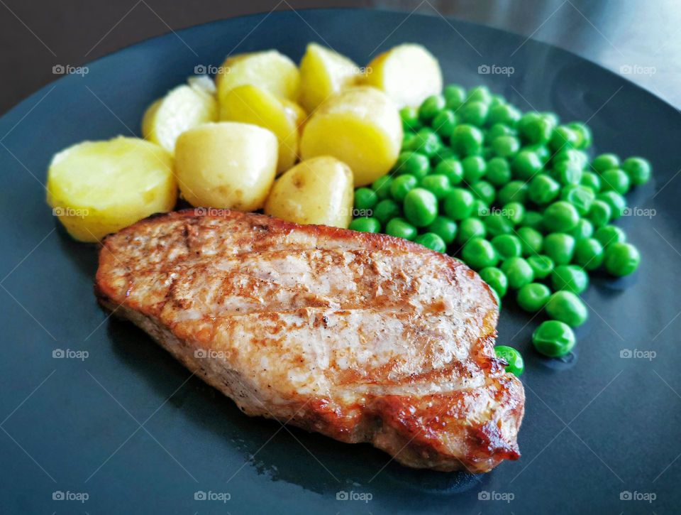 Grilled pork chop or pork steak with baby potatoes and peas. Selective focus at the piece of pork chop and copy space is at the blurry part of the photo.