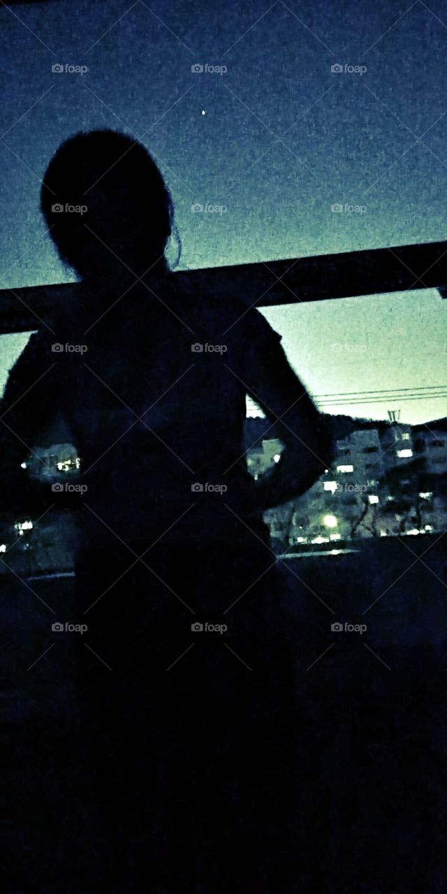 The silhouettes of a woman looking up  in the west side sky where a big star shine so bright among the other stars.