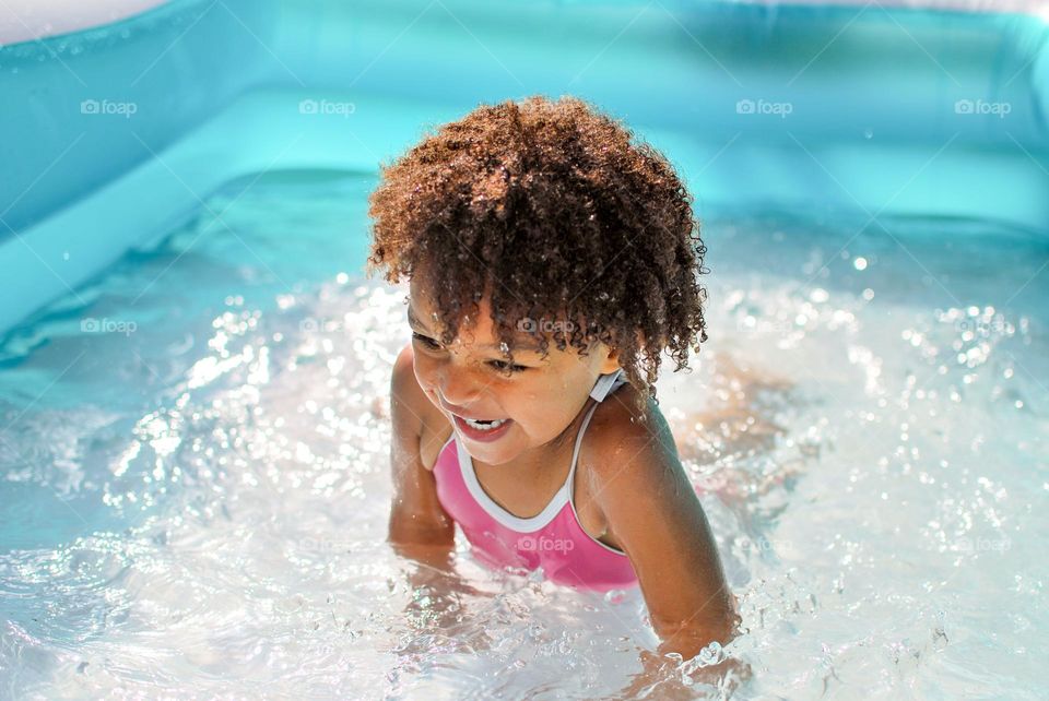 Cute little girl enjoying some playtime in a swimming pool during a hot summer day, looking for refreshment