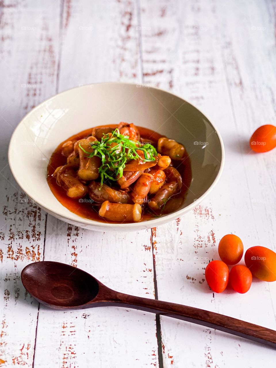 Octopus in spicy hot sambal in a ceramic bowl on a white wooden table top