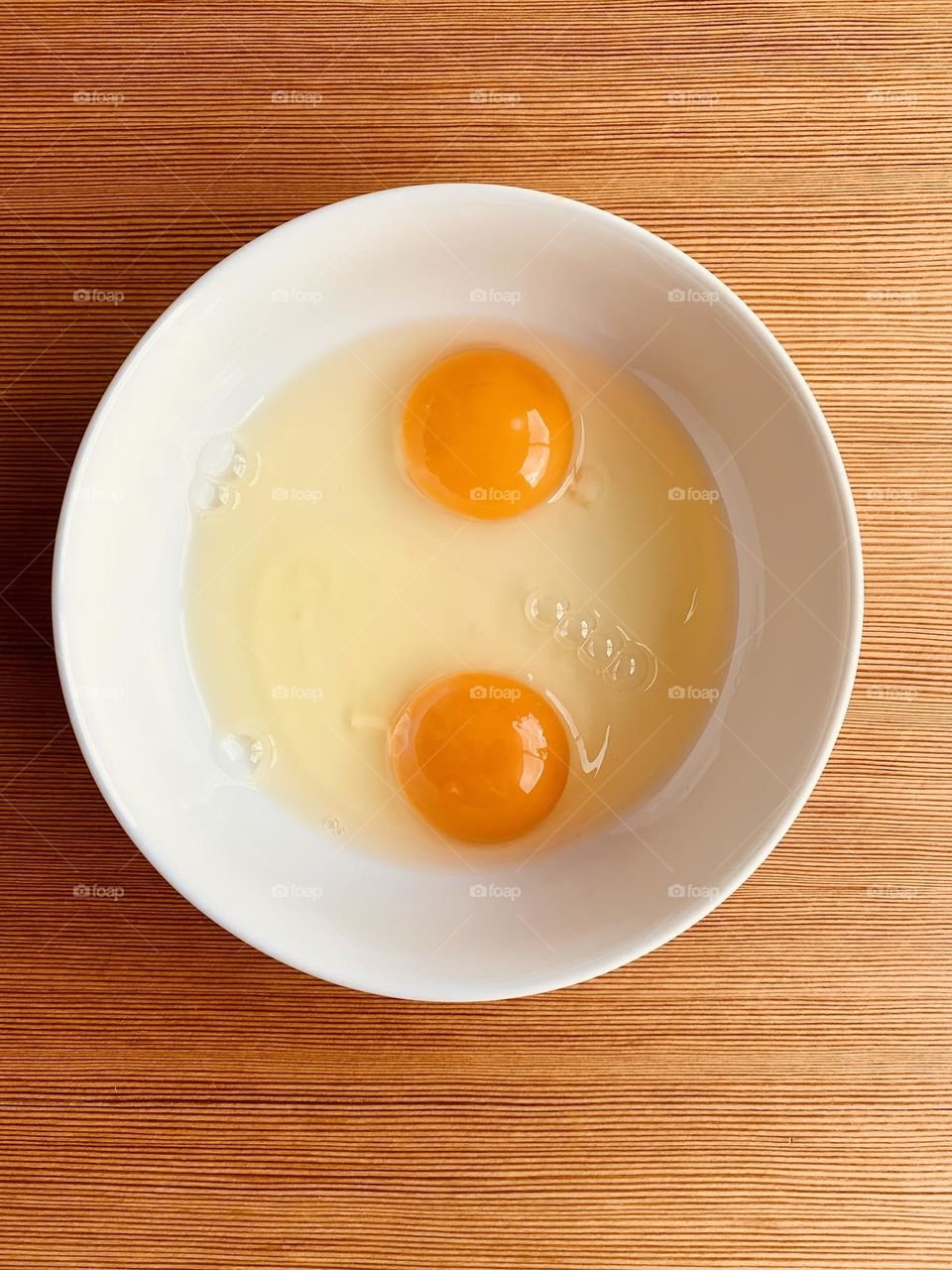 Yolks and egg whites in a white ceramic bowl on wooden surface from above 