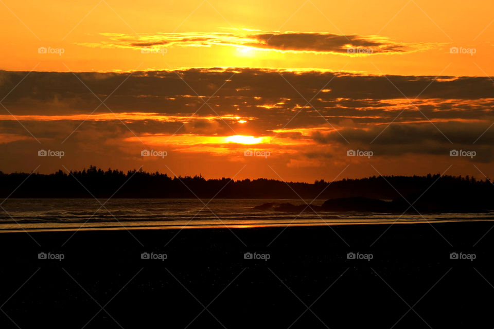 A brilliant orange sunset where the ocean meets the glistening beach