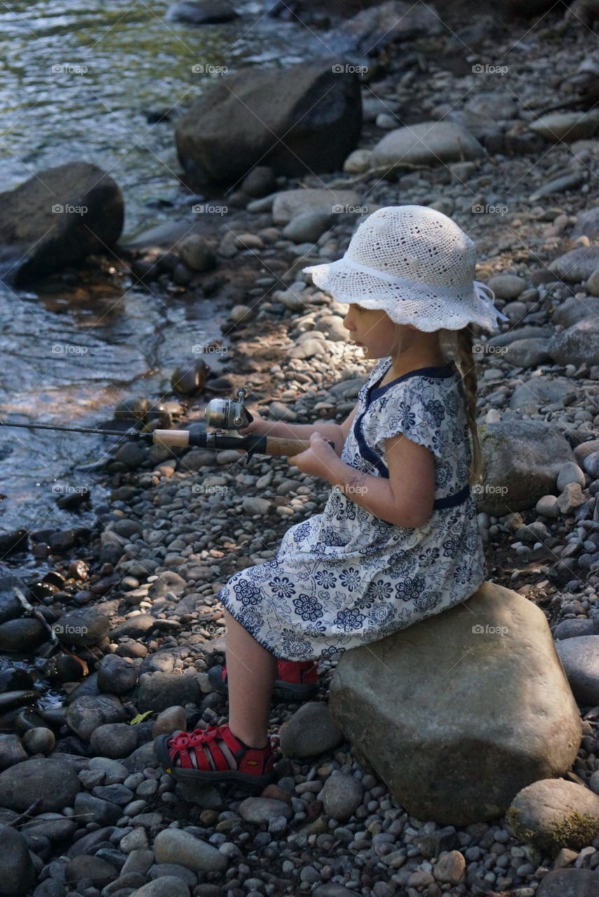 Little girl with long hair in a braid wearing a hat while fishing