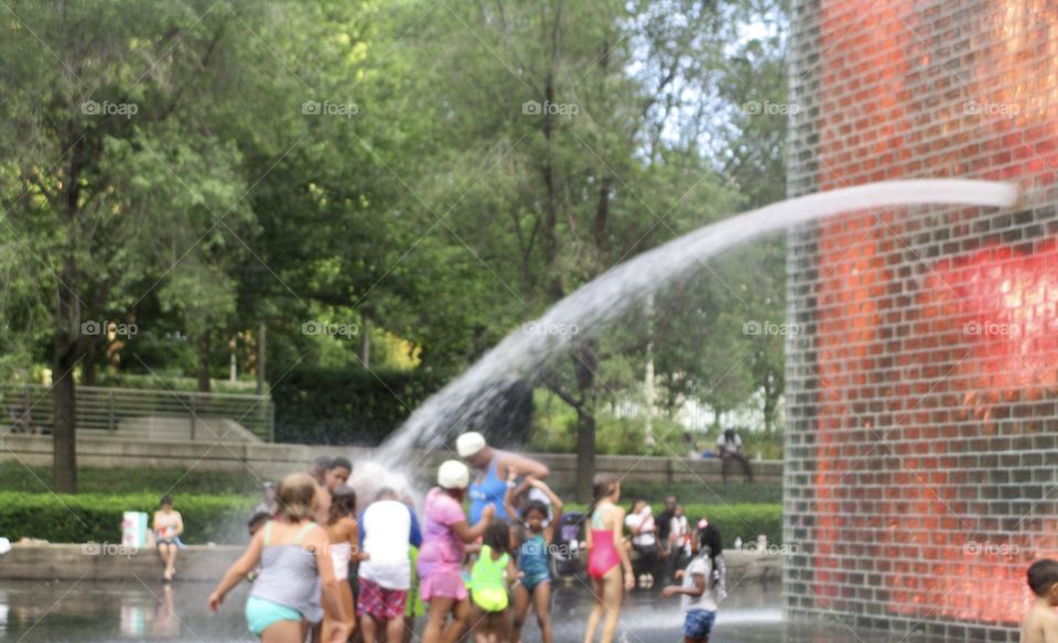 A stream of water coming from a wall, splashing on children in a city park