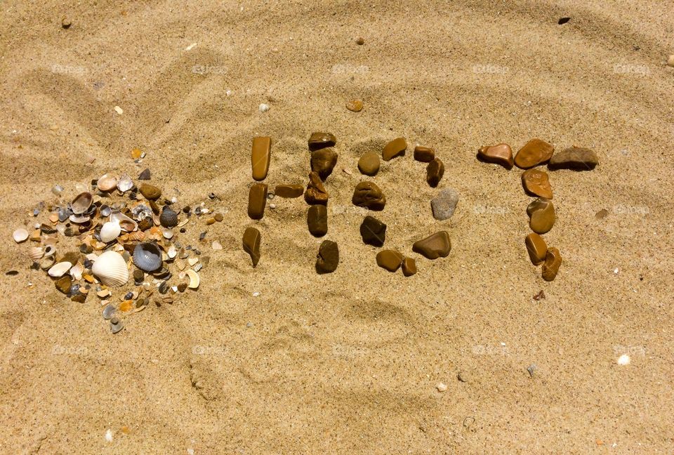 HOT letters with stones and shells on a sand