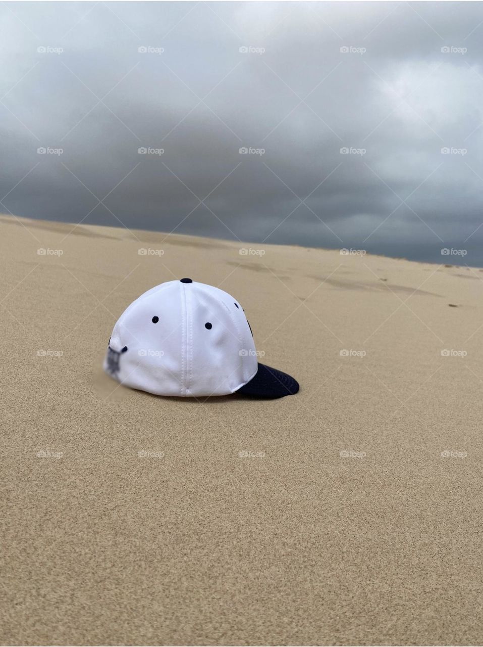 Baseball hat atop a sand dune. 