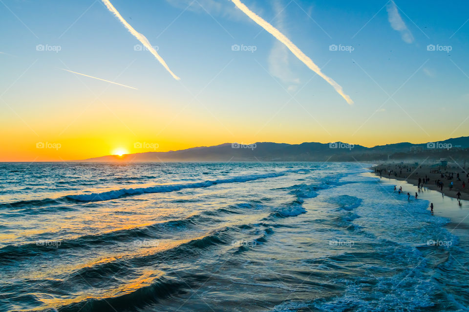 Sunset at Santa Monica Beach, California with a beautiful view of the waves and the mountains with a golden and blue sky. 