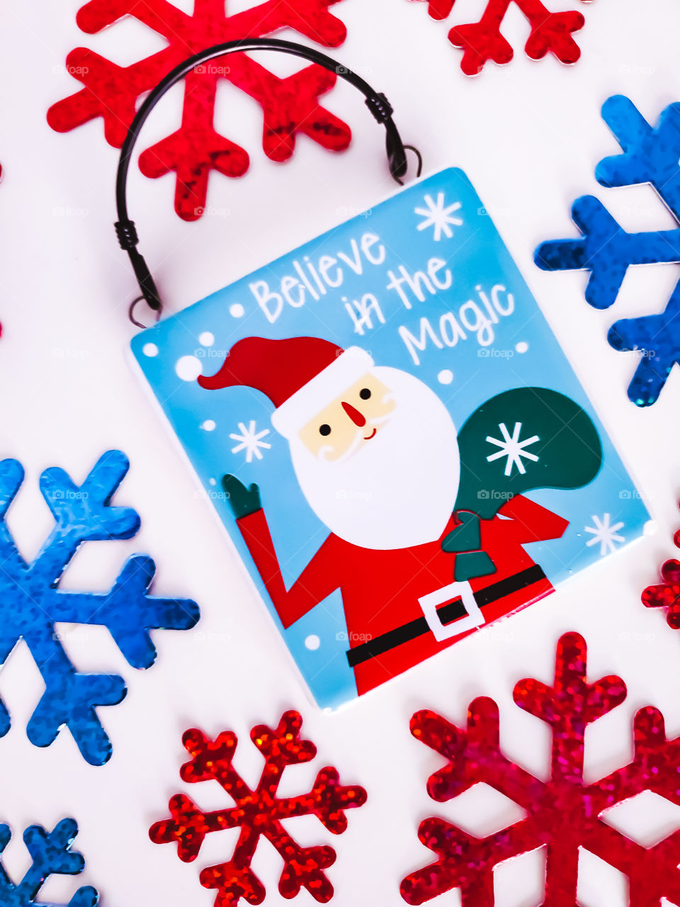 Believe in magic Christmas flatlay with Santa Clause surrounded by red and blue snowflakes on a white background.