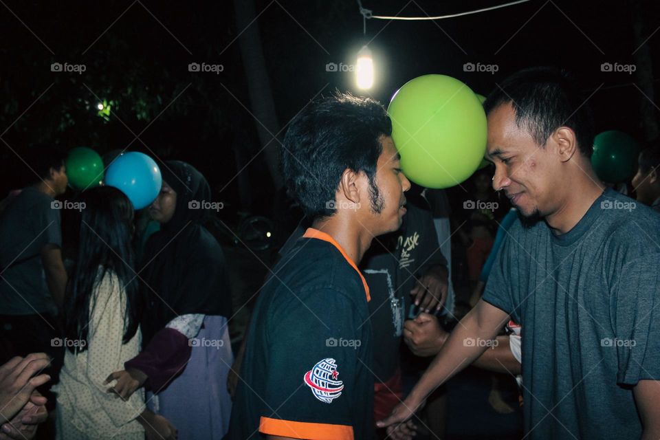 Close up of a group of men looking happy doing a dance game with balloons attached to their heads, a teamwork game to build a great team.