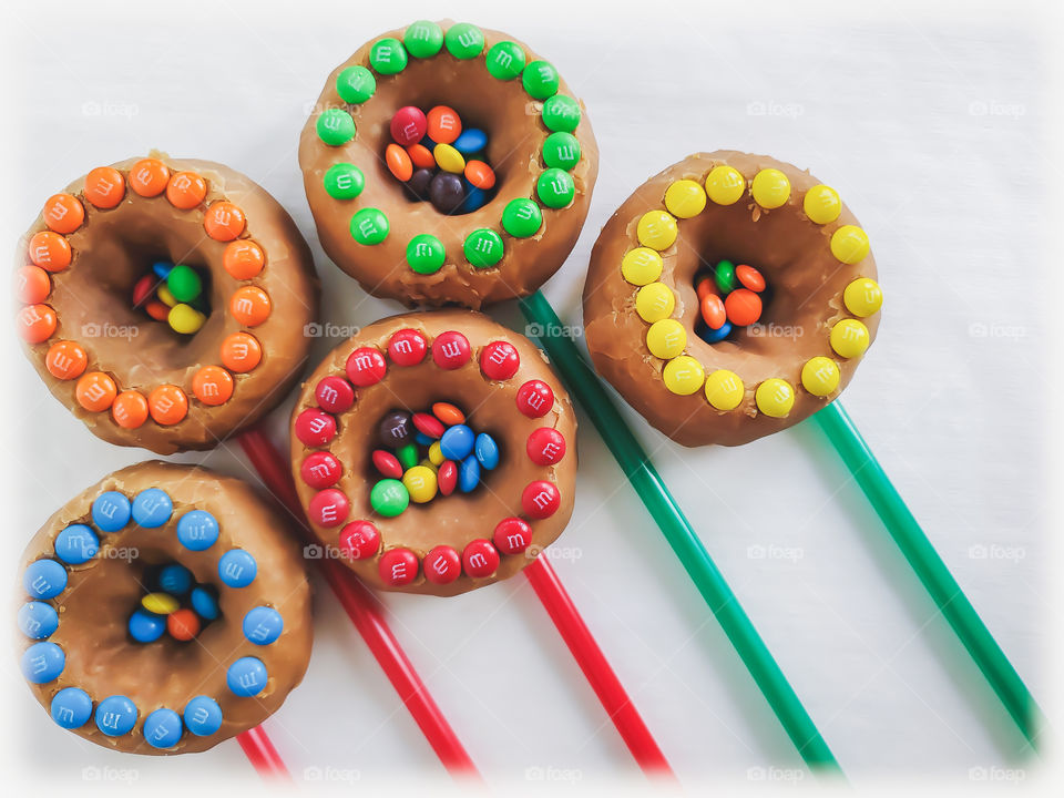 M&M minis decorated donuts filled with peanut M&Ms and mini M&Ms in the center, layed out in a creative bursting/shooting star or flower bouquet design on a white background.